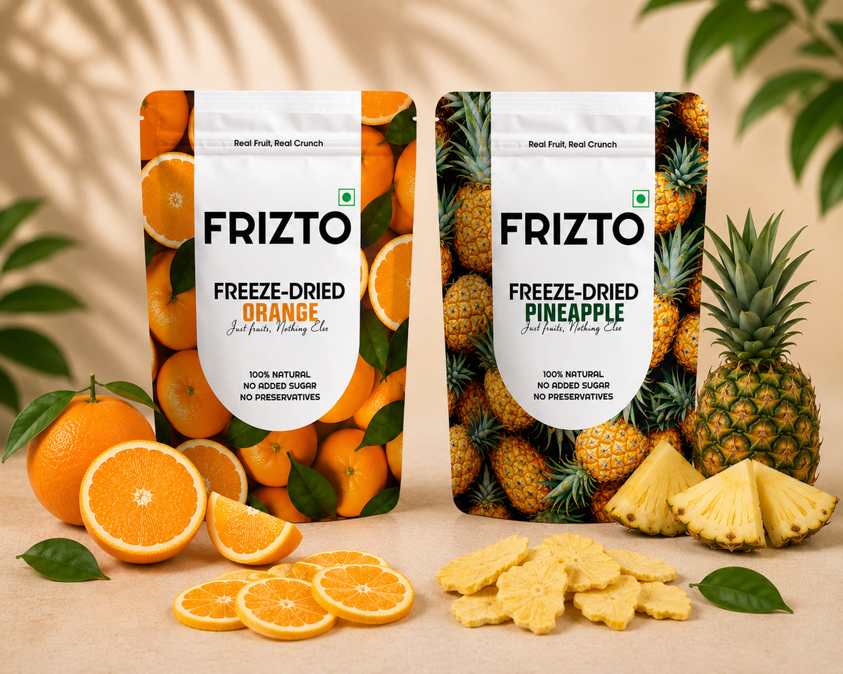 Two stand-up pouches of FRIZTO freeze-dried fruit snacks are shown on a beige surface with fruit props. The left pouch is labeled FRIZTO Freeze-Dried Orange and features orange imagery.